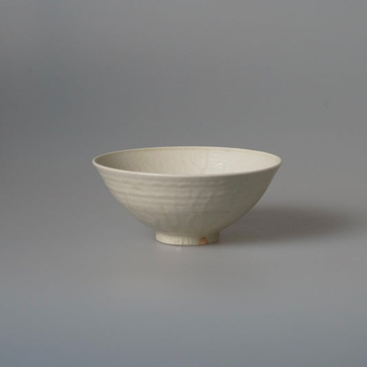 Shallow footed bowl in soft cream white with thin flaring walls, on pale grey.