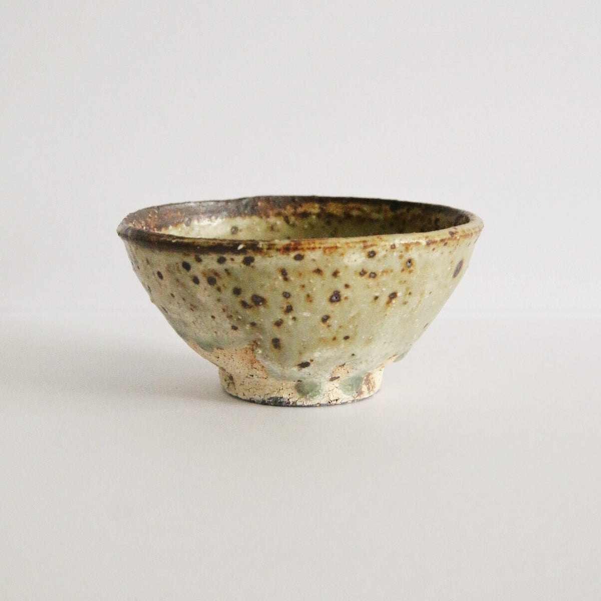 Footed cream rice bowl flecked with dark iron spots and a thin brown line around the rim.