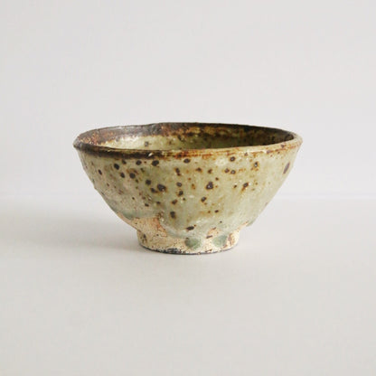 Footed cream rice bowl flecked with dark iron spots and a thin brown line around the rim.