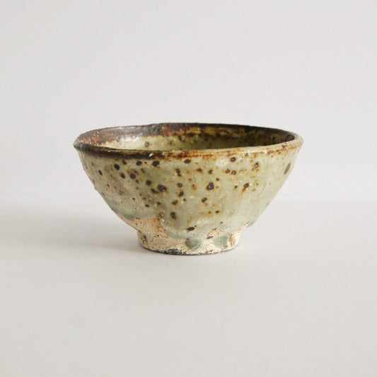 Footed cream rice bowl flecked with dark iron spots and a thin brown line around the rim.