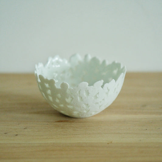 White porcelain bowl with a deeply torn, lace-like rim, on a light wooden table.
