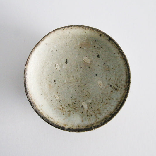 Round plate seen from above in speckled cream, its rim edged with dark iron marks.