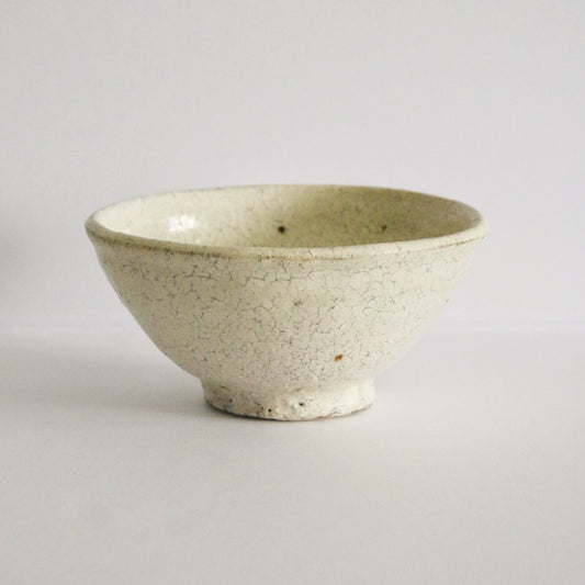 Plain cream rice bowl on a small foot, its speckled white slip catching the light.
