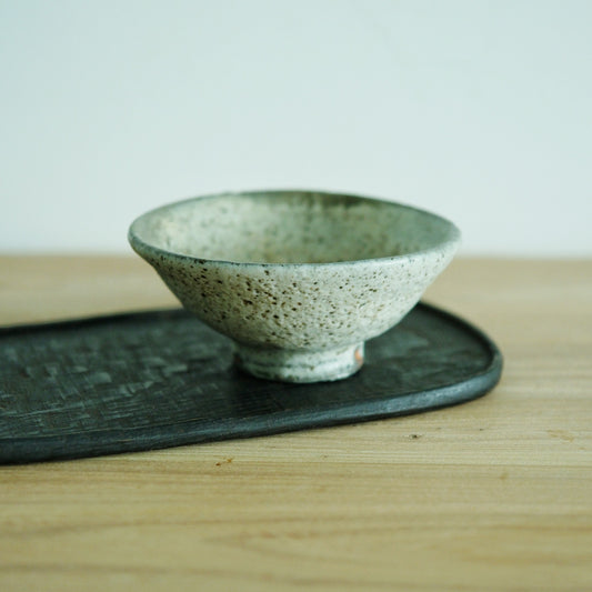 Shallow footed rice bowl in speckled sage green, standing on a dark board on a wooden table.