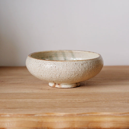 Round footed bowl in speckled cream with a warm brown glaze washing over the rim.