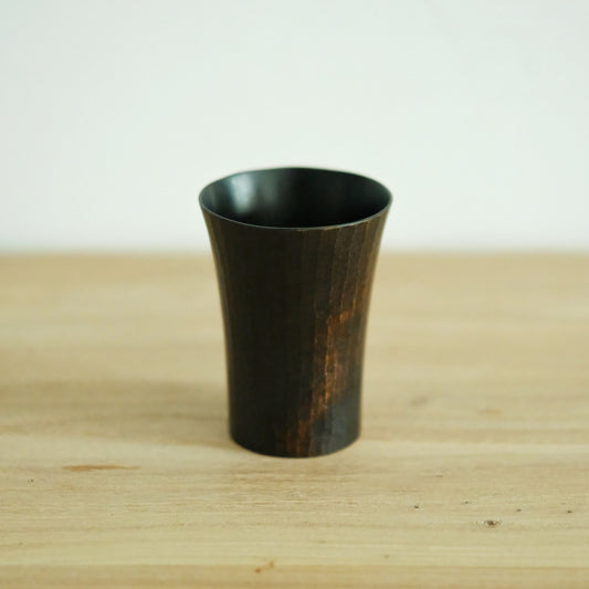 Straight-sided wooden cup finished in near-black, its grain showing faintly through, on pale timber.