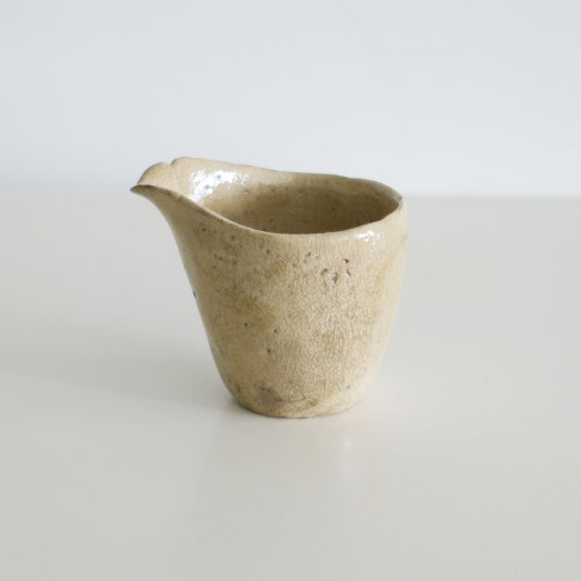 Small pouring bowl in speckled sandy cream with a sharply drawn spout, on white.