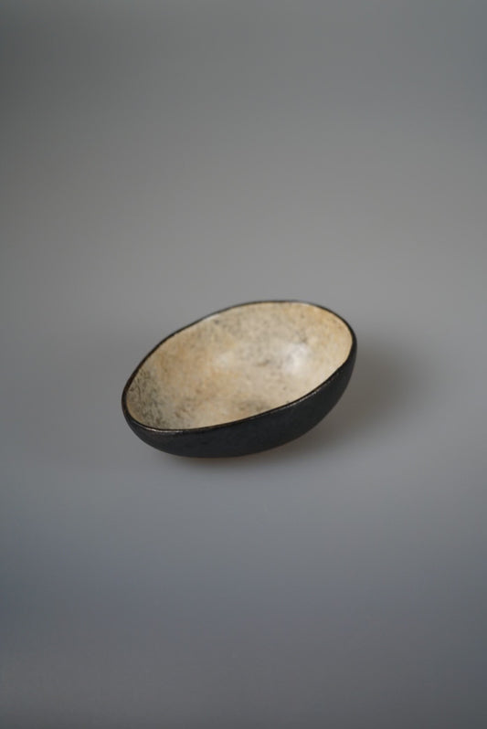 Shallow oval bowl with a black outer wall and a sandy cream glazed interior.