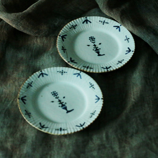 Two pale green plates with fluted rims, painted with small dark bird and arrow marks.