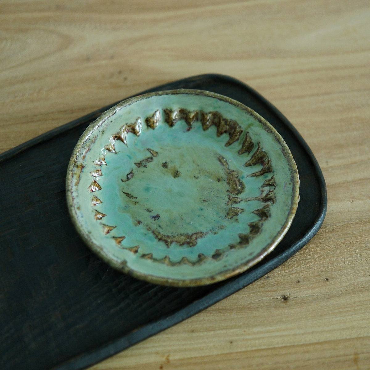 Small round dish with a turquoise glazed centre ringed by a toothed rust-brown border.