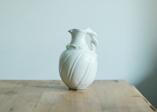 Small white porcelain vase with a fluted body and a softly pinched, uneven mouth, on wood.