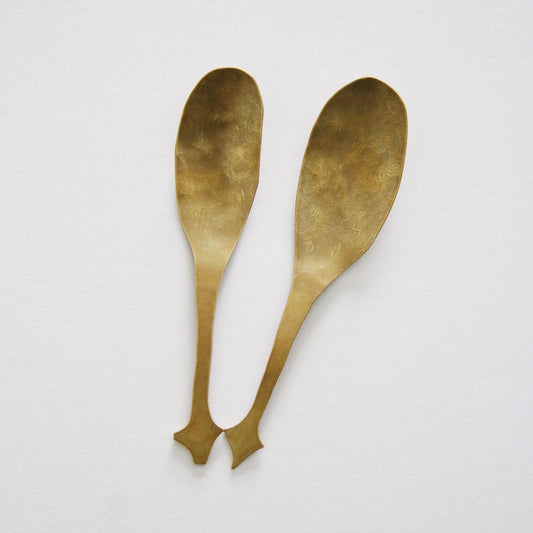 Two brass spoons with broad rounded bowls and forked tips at the end of each handle.