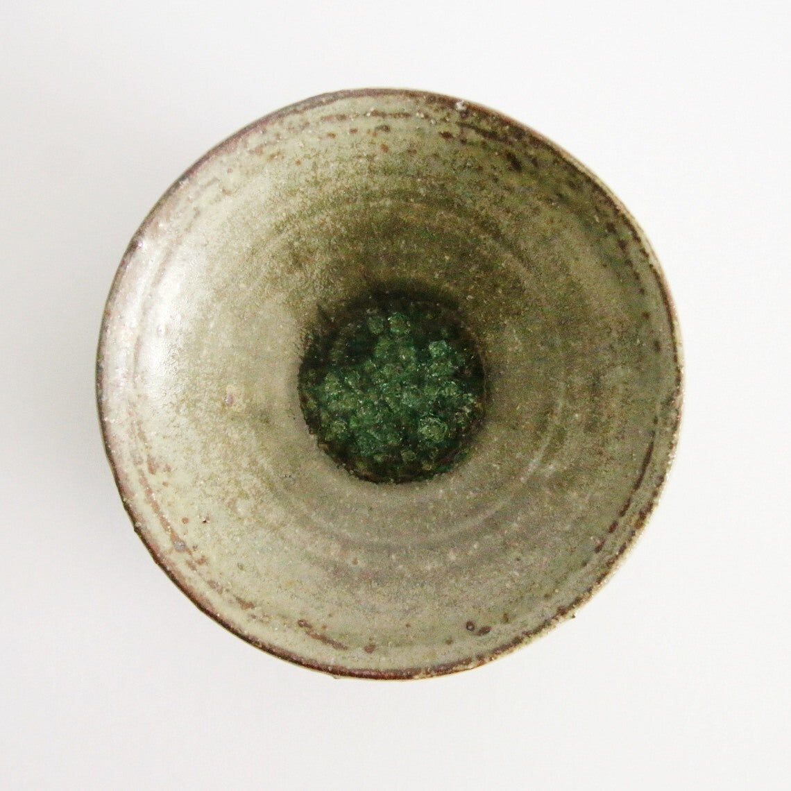 Deep cream bowl seen from above, its olive-green glazed well ringed by a rust-marked rim.