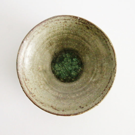 Deep cream bowl seen from above, its olive-green glazed well ringed by a rust-marked rim.