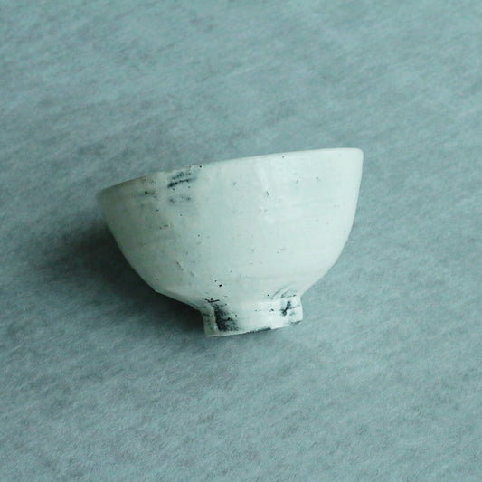 Deep bowl in pale mint green on a chipped foot, seen from above on soft blue cloth.