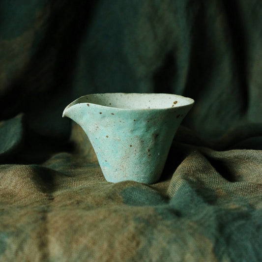 Small pale green pouring vessel with a flared rim and a soft drawn lip, on green cloth.