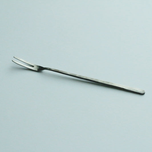 Slender two-pronged stainless steel fruit fork with a long plain handle, on a pale blue ground.