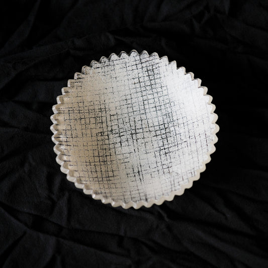 Round glass plate with a serrated edge and a fine grid pattern pressed into its frosted surface.