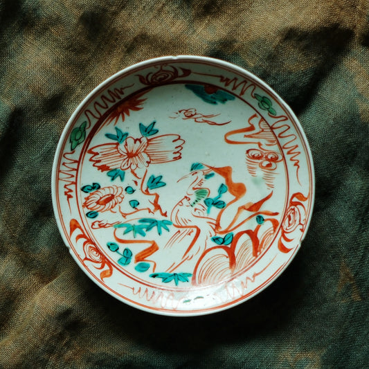 Cream plate painted in red and green line-work with flowering branches filling its whole face.