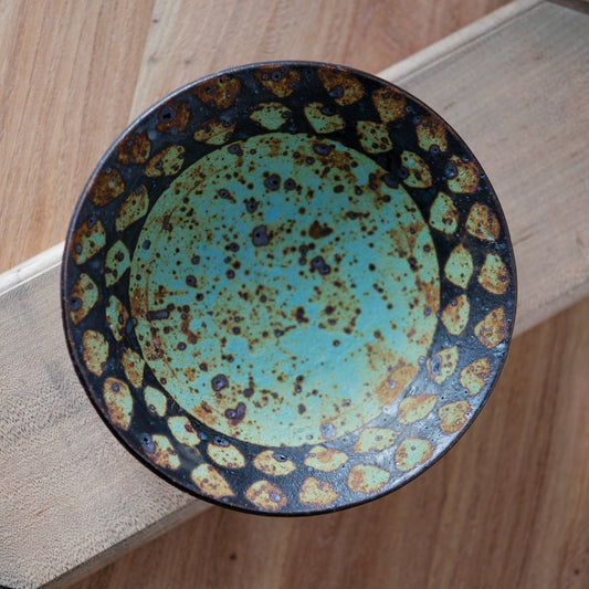 Round plate seen from above, a turquoise speckled centre ringed by a dark blue spotted border.