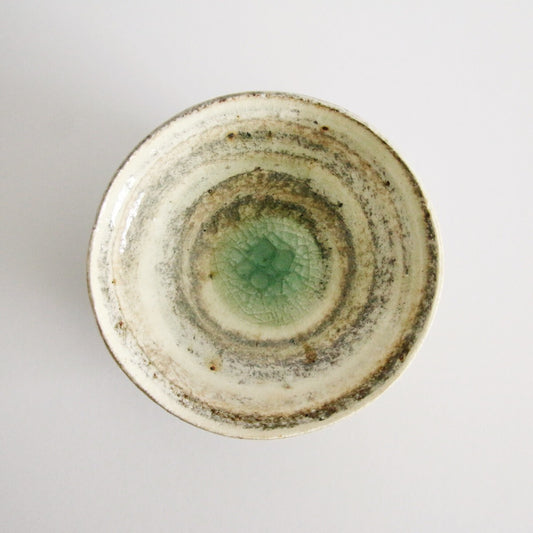 Cream bowl with a rust-flecked rim, concentric throwing rings and a soft green centre.