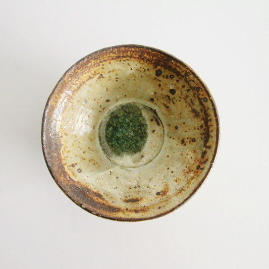 Shallow cream bowl with a heavily rust-flecked rim and a small jade green pool at the centre.