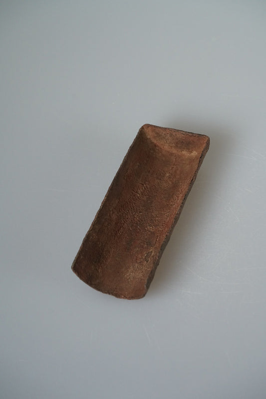 Curved tea scoop of lacquered cloth in deep russet brown, on a pale grey ground.
