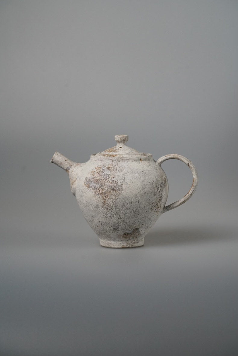Small white teapot with a rough chalky surface, a stubby spout and a looping handle.