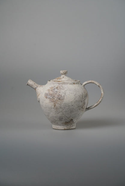 Small white teapot with a rough chalky surface, a stubby spout and a looping handle.
