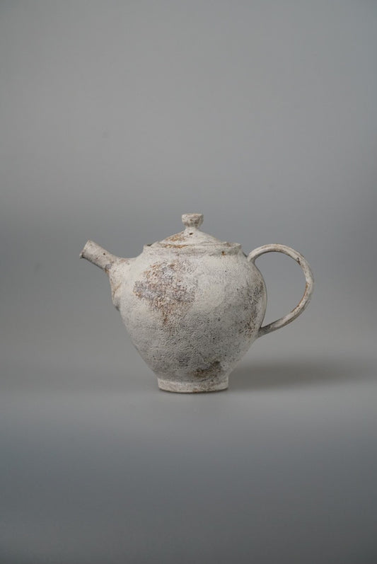 Small white teapot with a rough chalky surface, a stubby spout and a looping handle.