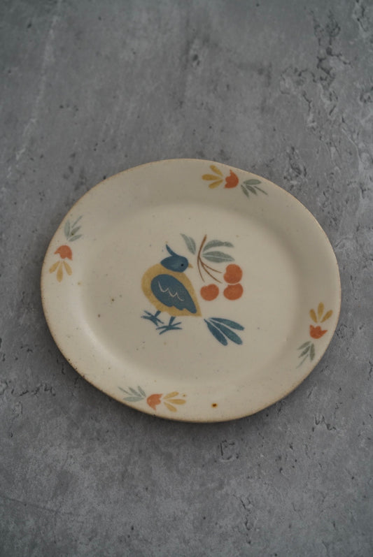 Oval cream plate painted with a small blue bird among orange berries and leaves.