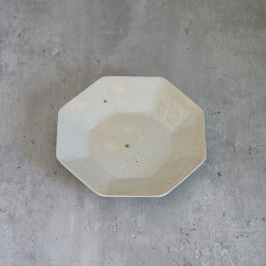 Octagonal plate in soft cream with a shallow well, seen from above on grey concrete.