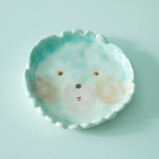 Small frilled plate in pale green painted with a simple round face and rosy cheeks.