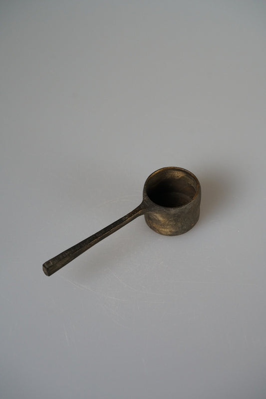 Long-handled wooden scoop with a deep round bowl in dark brown lacquer, on grey.