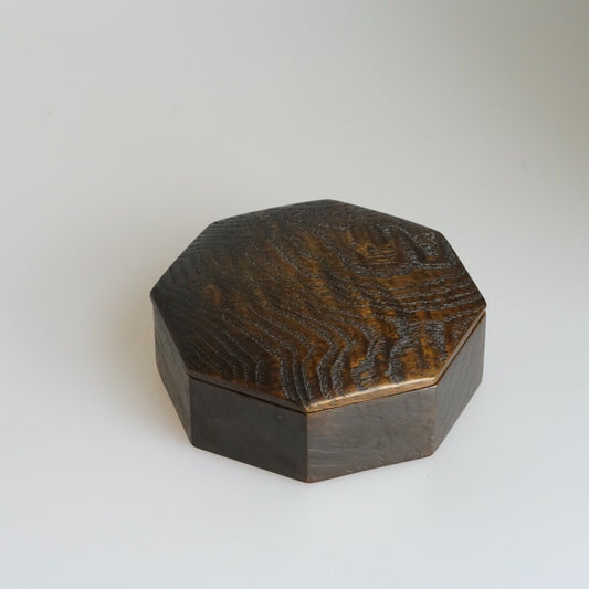 Octagonal lidded wooden box in warm brown lacquer, its faceted lid showing bold grain.