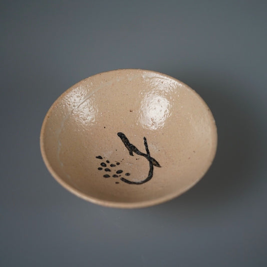 Round cream plate seen from above, brushed at its centre with a bold black stroke and dots.