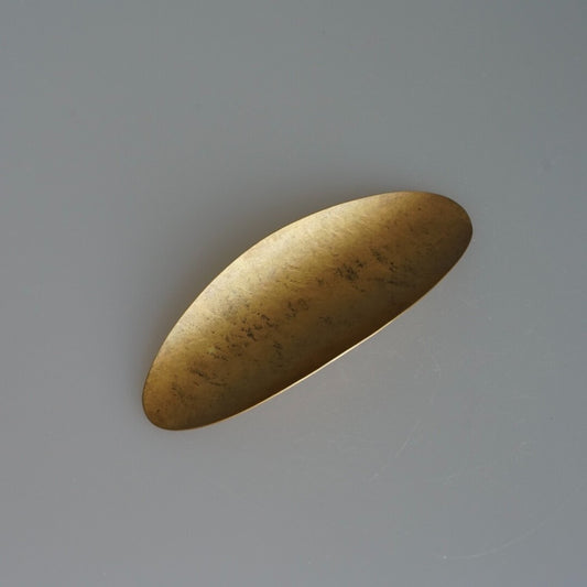 Broad brass tea scoop shaped like a long leaf, its hammered surface catching the light.