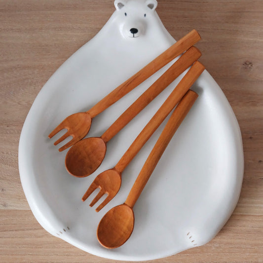 Four carved wooden spoons and forks laid on a white dish modelled with a small polar bear.