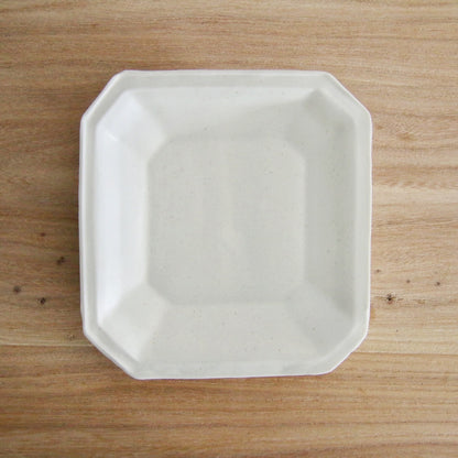 Octagonal white porcelain plate with a wide flat rim and softly cut corners, on a wooden table.