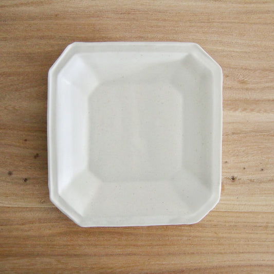 Octagonal white porcelain plate with a wide flat rim and softly cut corners, on a wooden table.