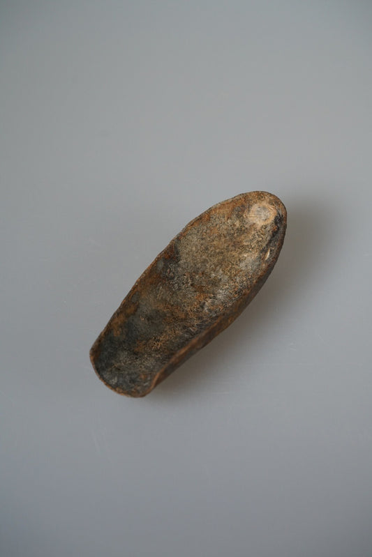 Curved tea scoop of lacquered cloth mottled in gold, green and brown, on pale grey.