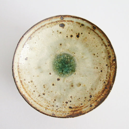 Shallow cream plate seen from above, speckled with iron and pooling to jade green at the centre.