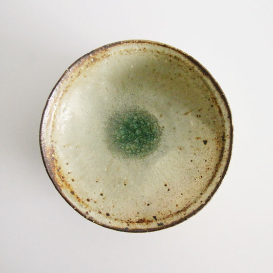 Cream plate with a rust-flecked rim and a small pool of jade green glaze at its centre.