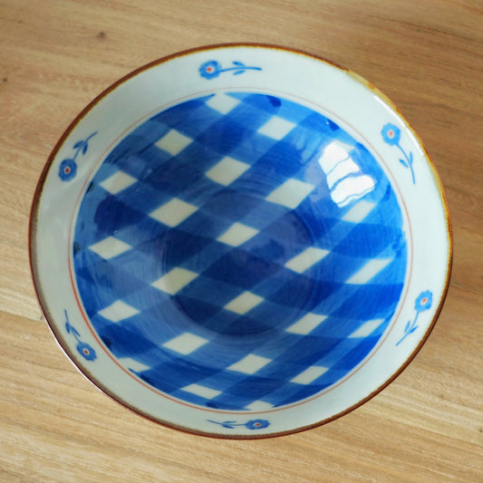 Shallow bowl seen from above, its well painted with a bold blue and white check and a flowered rim.