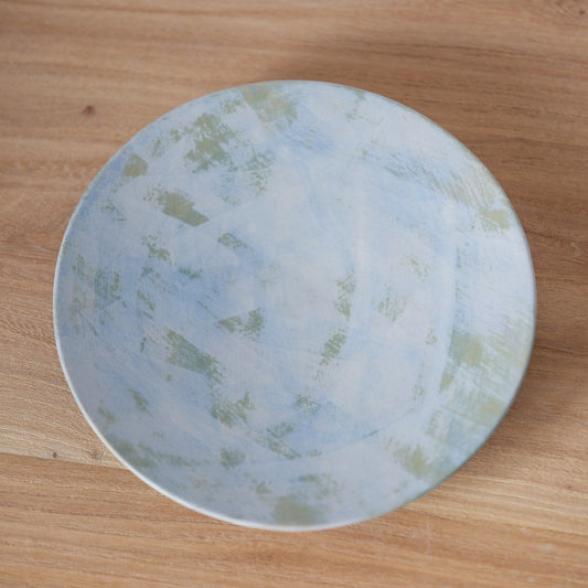 Round plate washed in soft sky blue with pale green cloud-like patches across its face.