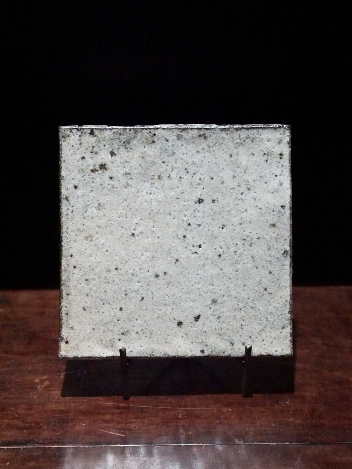 Square wood-fired dish in mottled white and grey with dark speckles, propped upright on a stand.