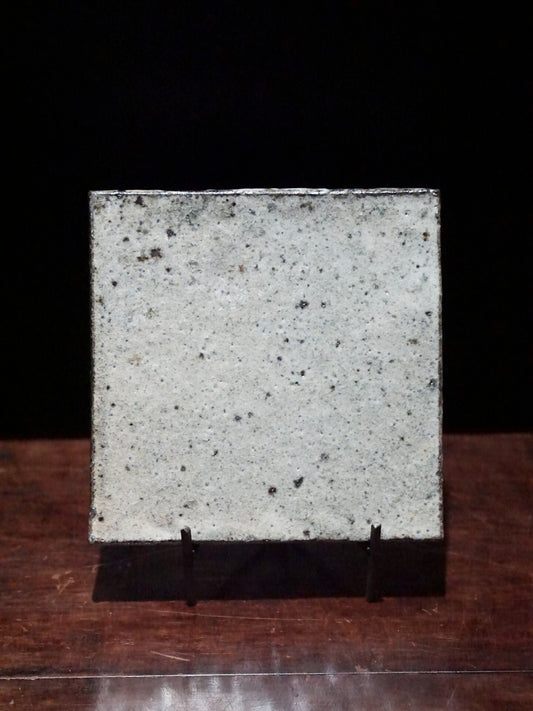 Square wood-fired dish in mottled white and grey with dark speckles, propped upright on a stand.