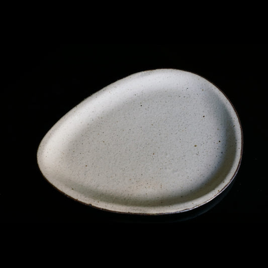 Smooth pebble-shaped tray in speckled off-white, lit softly against a black background.