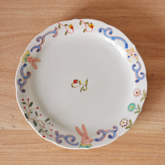 White plate with a scrolling painted border of rabbits, birds and flowers in soft blue and red.