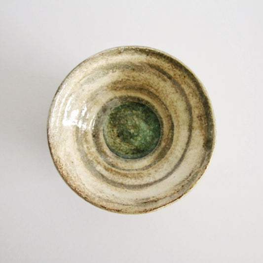 Conical cream bowl seen from above, ringed with throwing lines and green glaze gathered at its base.